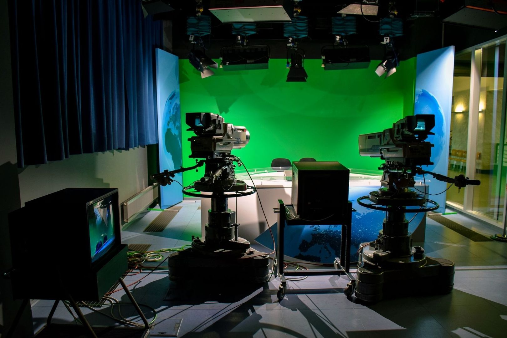 Kaksi televisiokameraa vihreäkangasstudiossa lähetyspöydän edessä